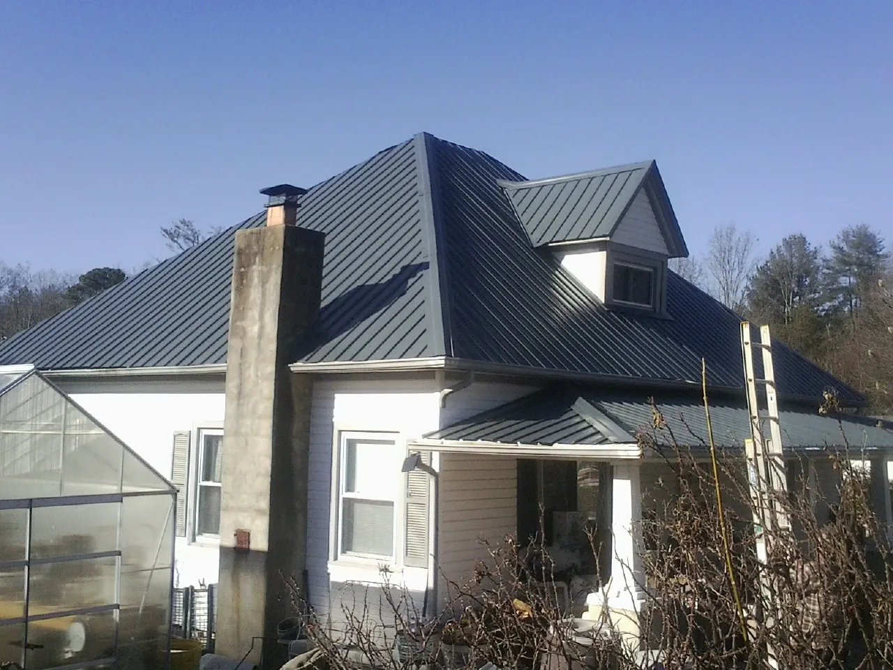 Dark blue standing seam metal roof on a white farmhouse with dormer — Slate & Tile Roof Repair by Roofing Brothers in Tolovana Park