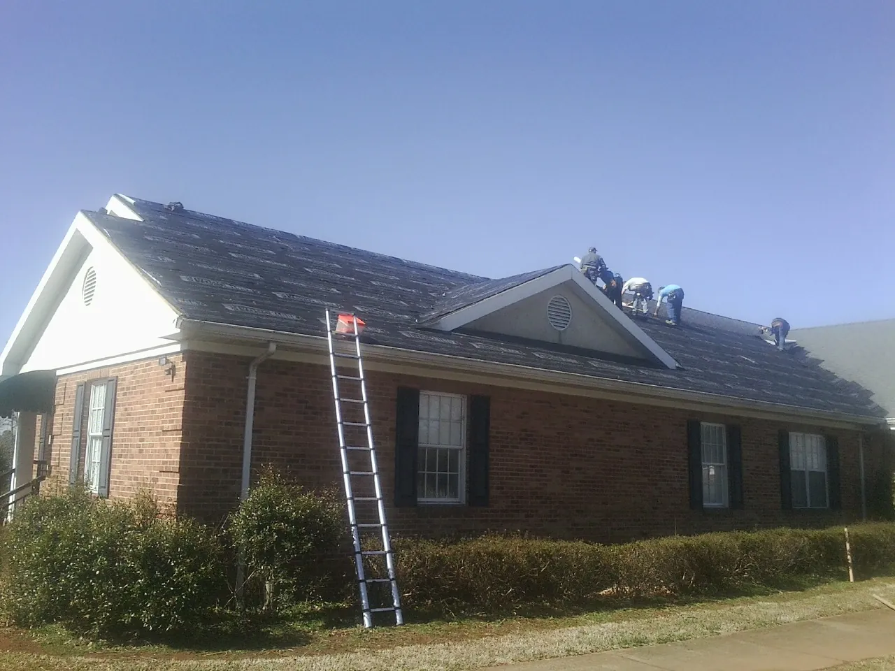Crew tearing shingles off a brick ranch roof with a ladder set — Metal Roof Repair work by our crew in Tolovana Park