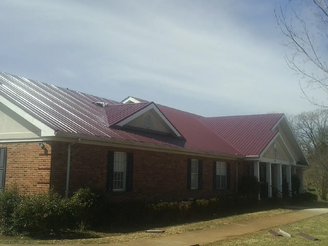 Red metal roof with gabled entries on a long brick building, from a Hail Damage Roof Repair job in Tolovana Park
