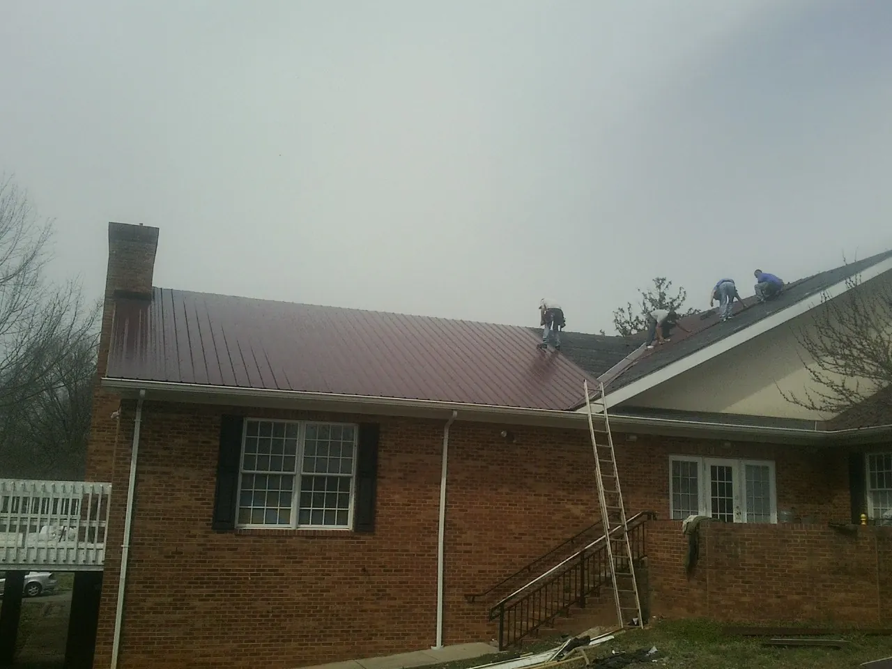 Crew setting red metal roofing panels on a brick home in Tolovana Park