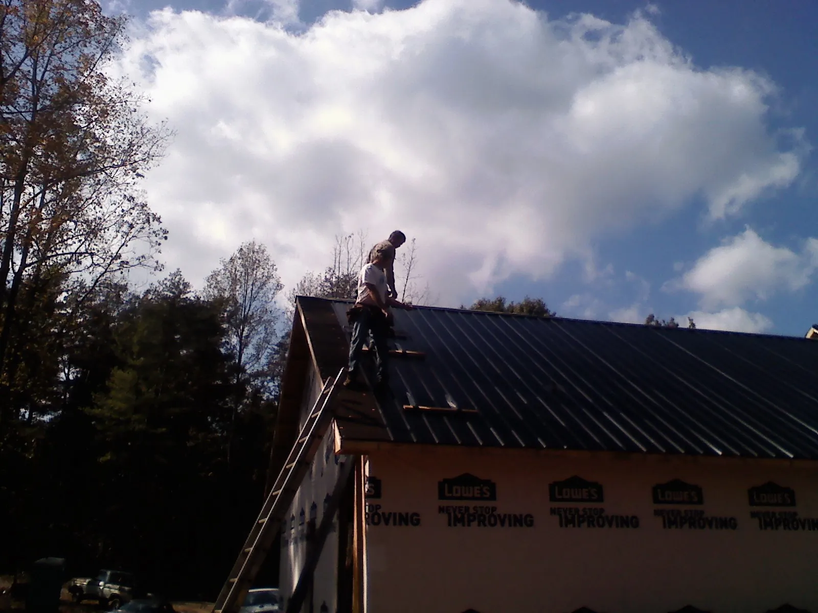 Roofer fastening dark metal panels high against a cloudy sky, from a Roof Inspection job in Tolovana Park