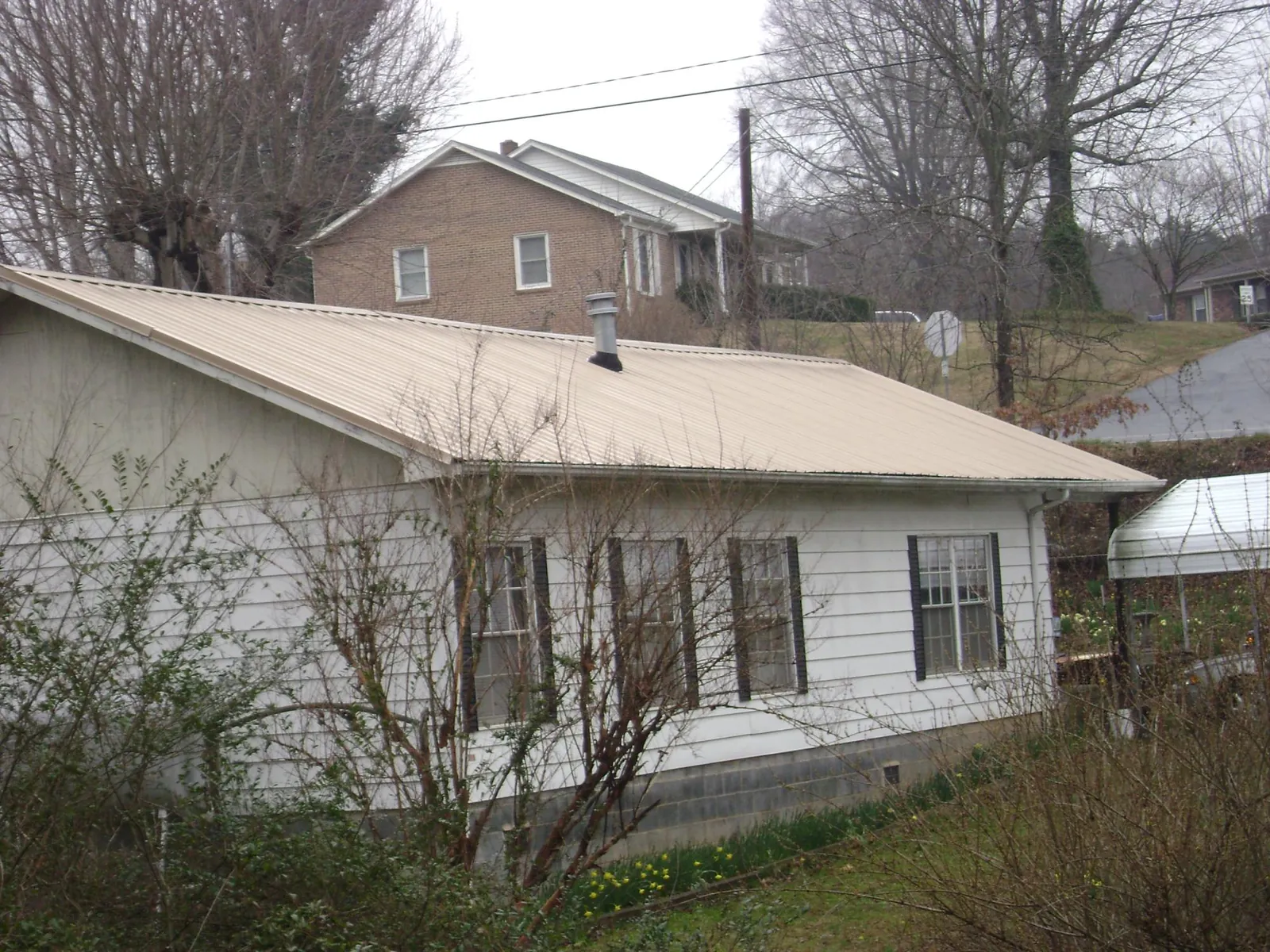 Tan metal roof on a white sided house set into a hillside — Commercial Roofing by Roofing Brothers in Tolovana Park